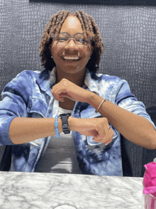 a woman wearing a blue tie dye shirt and a black watch smiles at the camera