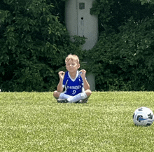 a young boy wearing a thunder jersey sits on the grass next to a soccer ball