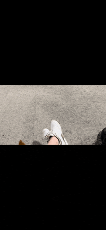 a person wearing white sneakers is standing on a sidewalk