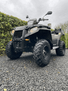 a polaris atv is parked on gravel in front of a hedge