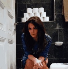 a woman in a blue dress sits on a toilet next to a pile of toilet paper