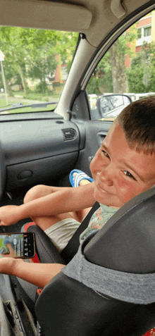 a young boy sits in a car seat looking at a phone