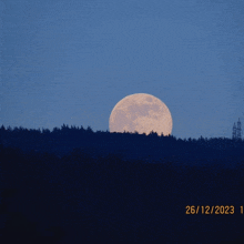 a full moon rises over a forest with the date 26/12/2023 at the bottom