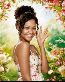 a woman in a floral dress is smiling and waving in front of flowers