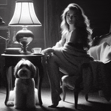 a woman sits in a chair next to a lamp and a small dog