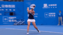 a woman is swinging a tennis racket on a tennis court in front of a blue wall with chinese writing on it