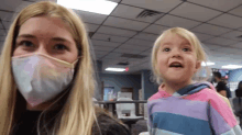 a woman wearing a mask stands next to a little girl in a striped shirt