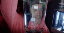 a person is holding a glass of water with a reflection of a woman 's face in it .