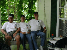 three men sitting on a porch swing with one wearing a hat that says ' army '