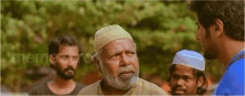 a group of men are standing around talking to each other . one of the men is wearing a white hat .