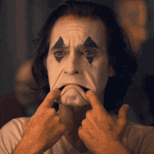 a man with joker makeup on his face making a face with his hands