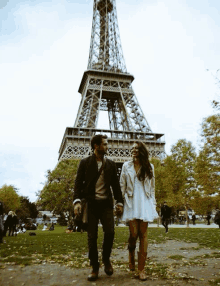 a man and a woman are holding hands in front of the eiffel tower