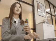 a woman in a suit is sitting at a desk with a bottle of water and a sign that says bins