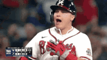 a baseball player is standing on the field with his hands on his chest and a scoreboard in the background .