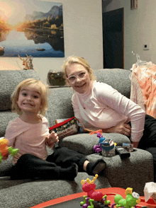 a woman and a little girl sit on a couch with toys and a purse that says minnie mouse on it