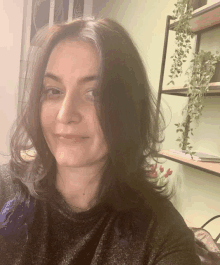 a woman with dark hair is smiling in front of a shelf