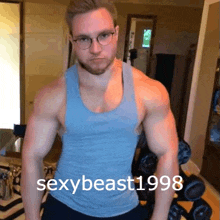 a muscular man wearing glasses and a blue tank top is standing next to a dumbbell rack .