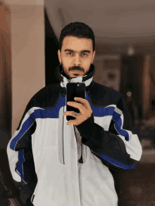 a man in a blue and white jacket takes a selfie with his phone