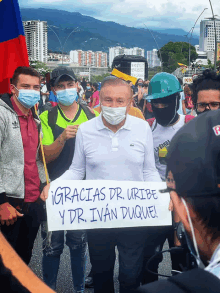 a man wearing a mask holds a sign that says gracias dr. uribe y dr. ivan duquel