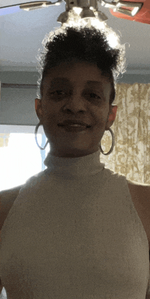 a woman wearing a white turtleneck and hoop earrings smiles