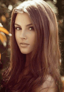 a close up of a woman 's face with long brown hair and a flower in the background .