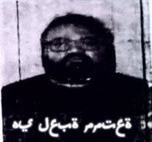 a black and white photo of a man with glasses and a beard with arabic writing .