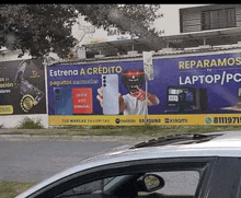 a car is driving past a billboard that says reparamos tu laptop / pc