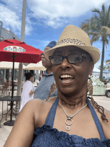 a woman wearing a hat and glasses is smiling in front of a red umbrella that says rick 's