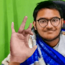 a man wearing glasses and a blue scarf is making an ok sign with his hand