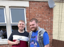 two men are standing in front of a brick building .