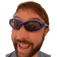 a man with a beard wearing blue sunglasses is smiling .