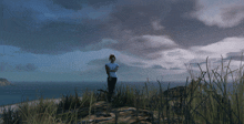 a woman in a white shirt stands on a hill overlooking a body of water