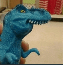 a person is holding a blue toy dinosaur with a large mouth