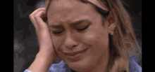 a woman is crying while holding her head with her hand .