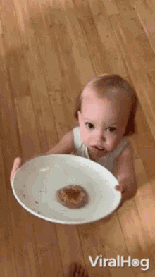 a little girl is holding a white plate with a cookie on it and the words viralhog on the bottom right