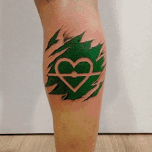 a person has a tattoo of a heart under a green leaf on their leg .