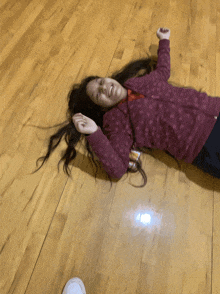 a girl in a purple jacket is laying on her back on the floor