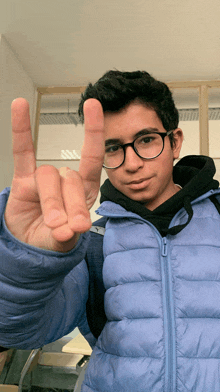 a young man wearing glasses and a blue jacket is giving a peace sign