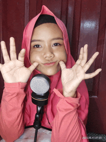 a girl in a pink hijab stands in front of a microphone with her hands in the air