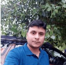 a man in a blue shirt stands in front of a tree and a car