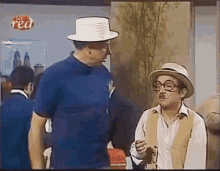 two men wearing hats and glasses are standing next to each other and talking in a room .