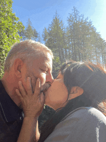 a man and a woman kissing in front of trees