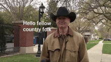 a man wearing a cowboy hat is standing on a sidewalk and talking into a microphone ..