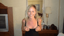 a woman in a black tank top is smiling in front of a mirror .