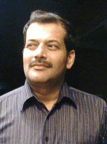 a man with a mustache wearing a striped shirt looks at the camera