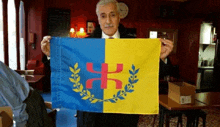 a man is holding a blue and yellow flag with a red symbol on it