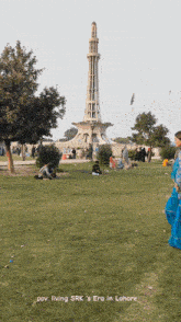 a woman in a blue dress stands in a park with a tower in the background and the words living srk 's era