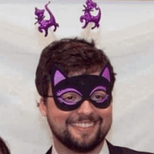 a man with a beard is wearing a cat mask with purple ears and horns .