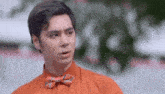 a man wearing an orange shirt and a red bow tie is looking at the camera .