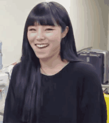 a woman with long black hair is smiling and wearing a black top